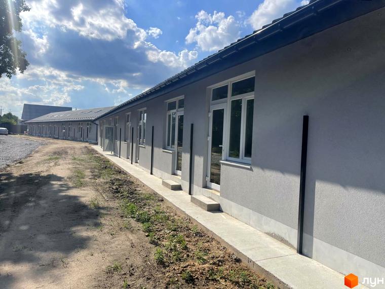 Зовнішній вигляд житлового комплексу Oak-Park з сірими фасадами та великими вікнами, що виходить на ґрунтову дорогу та зелену зону.