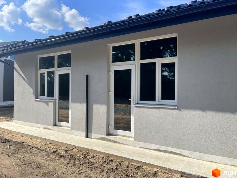 Зовнішній вигляд новобудови Таунхауси Оак-Парк з білими вікнами та сірою штукатуркою. Поруч розташована прибудинкова територія з піском та бетонною доріжкою.