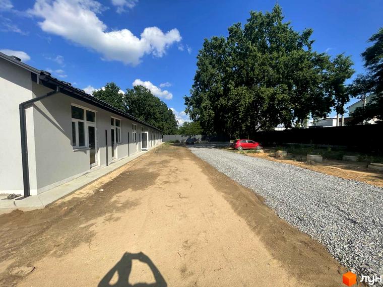 Таунхауси Оак-Парк: одноповерхові будівлі з сірими фасадами та білими вікнами, поруч гравійна дорога та зелені дерева.