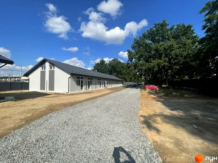 Будівля таунхаусів Оак-Парк з сірим дахом та білими стінами, розташована на ділянці з гравійним покриттям та зеленими деревами.