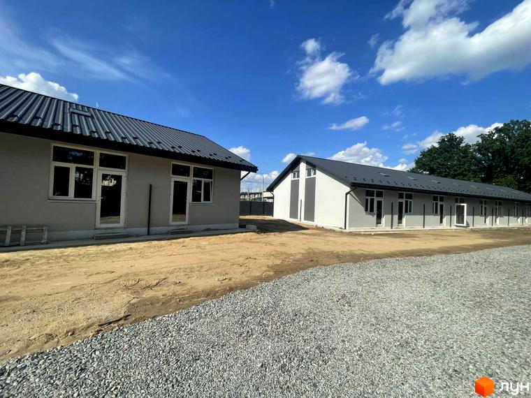 Будівельний проєкт Oak Park: сірі фасади будівель з темними дахами та вікнами. Територія навколо засипана гравієм та піском.