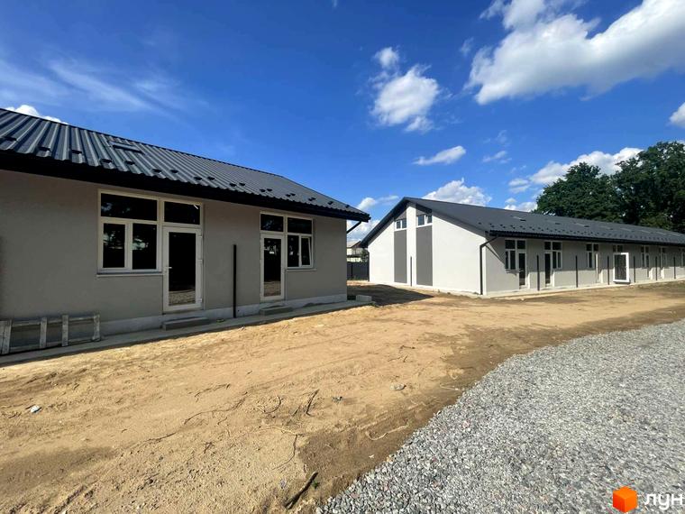 Новобудова Таунхауси Оак-Парк з сірими фасадами та темним дахом на тлі блакитного неба з хмарами. Прибудинкова територія з гравійним покриттям та піщаною ділянкою.