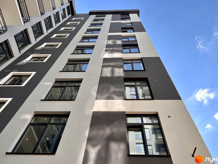 Фасад житлового комплексу Хмельницький з великою кількістю вікон на тлі блакитного неба. Будинок має сіро-білу кольорову гаму.