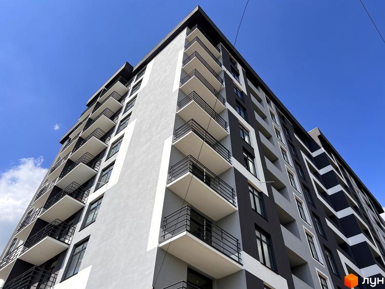 Фасад житлового комплексу Хмельницький з балконами та вікнами на тлі блакитного неба. Зовнішній вигляд новобудови з сірими та чорними елементами.