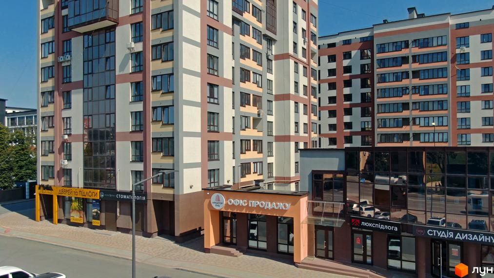 Зовнішній вигляд фасаду житлового комплексу Варшавський мікрорайон з вікнами та балконами. На першому поверсі розташовані комерційні приміщення з вивісками.