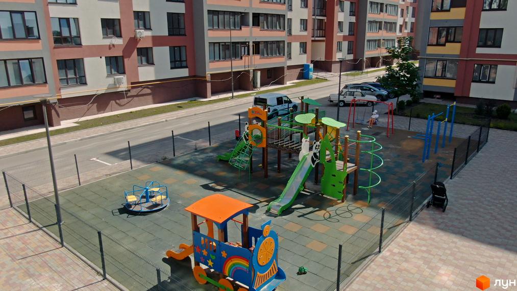 Зовнішній вигляд багатоповерхових будинків ЖК Варшавський мікрорайон. На прибудинковій території дитячий майданчик з гірками, гойдалками та потягом.