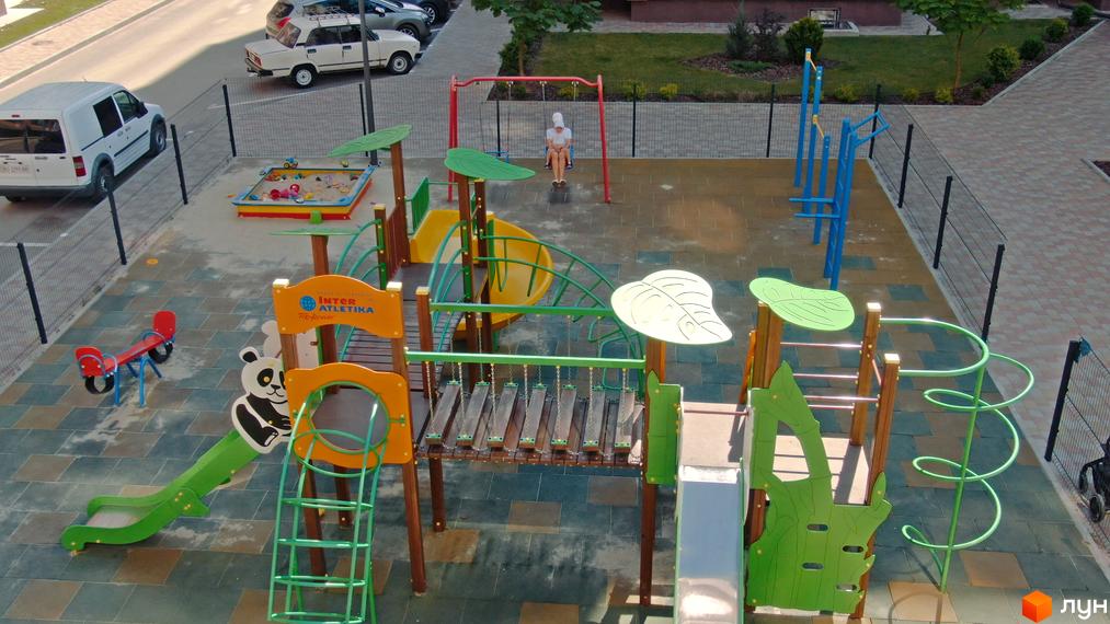 Дитячий майданчик у житловому комплексі Варшавський мікрорайон з гірками, гойдалками та пісочницею. На території є парковка та зелені насадження.