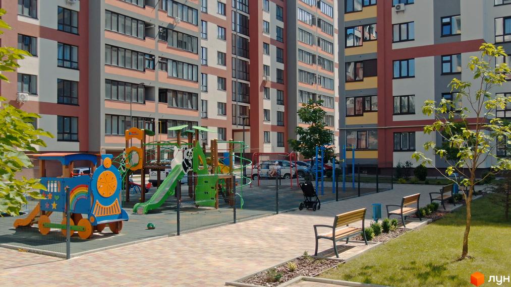 Житловий комплекс Варшавський мікрорайон: сучасні багатоповерхові будинки з яскравим фасадом та облаштований дитячий майданчик з потягом та гірками.
