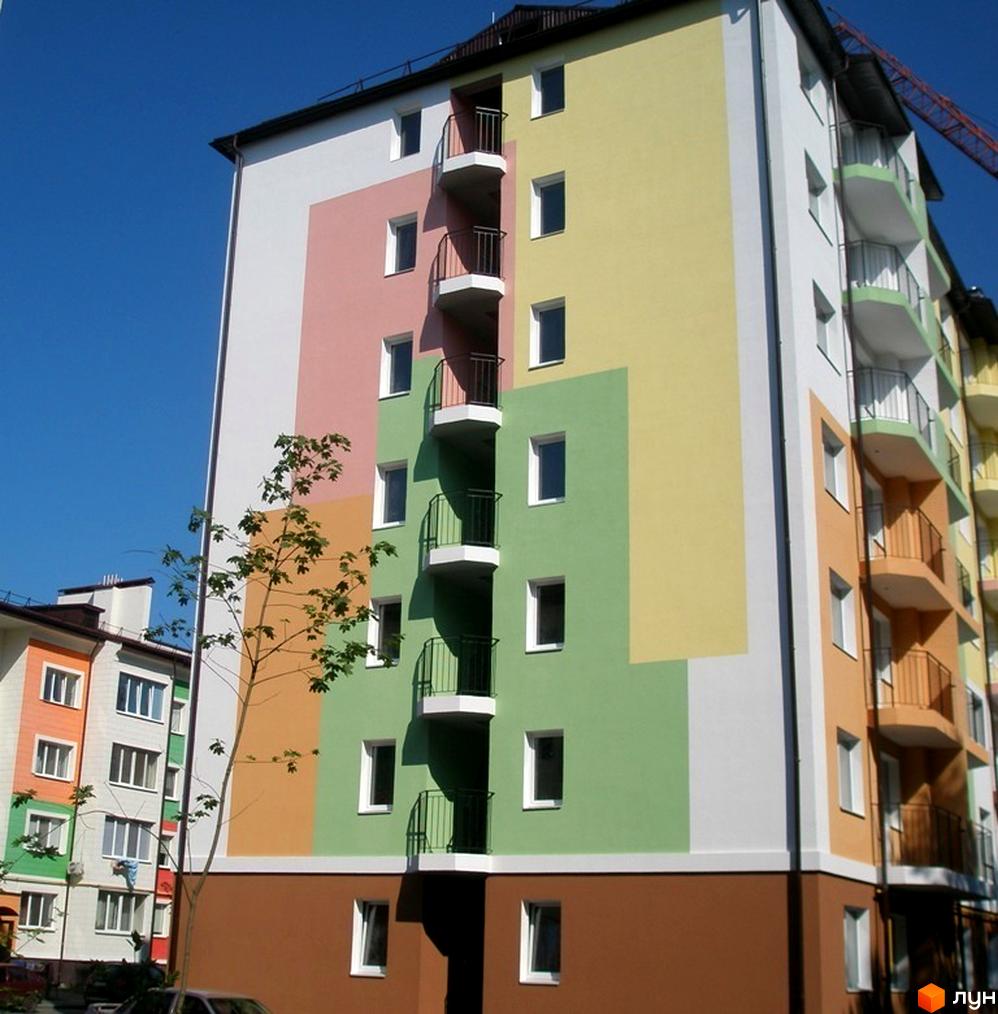 Житловий комплекс Ягода: яскравий фасад будинку з балконами та вікнами. Навколо будинку видно дерева та сусідні будівлі.