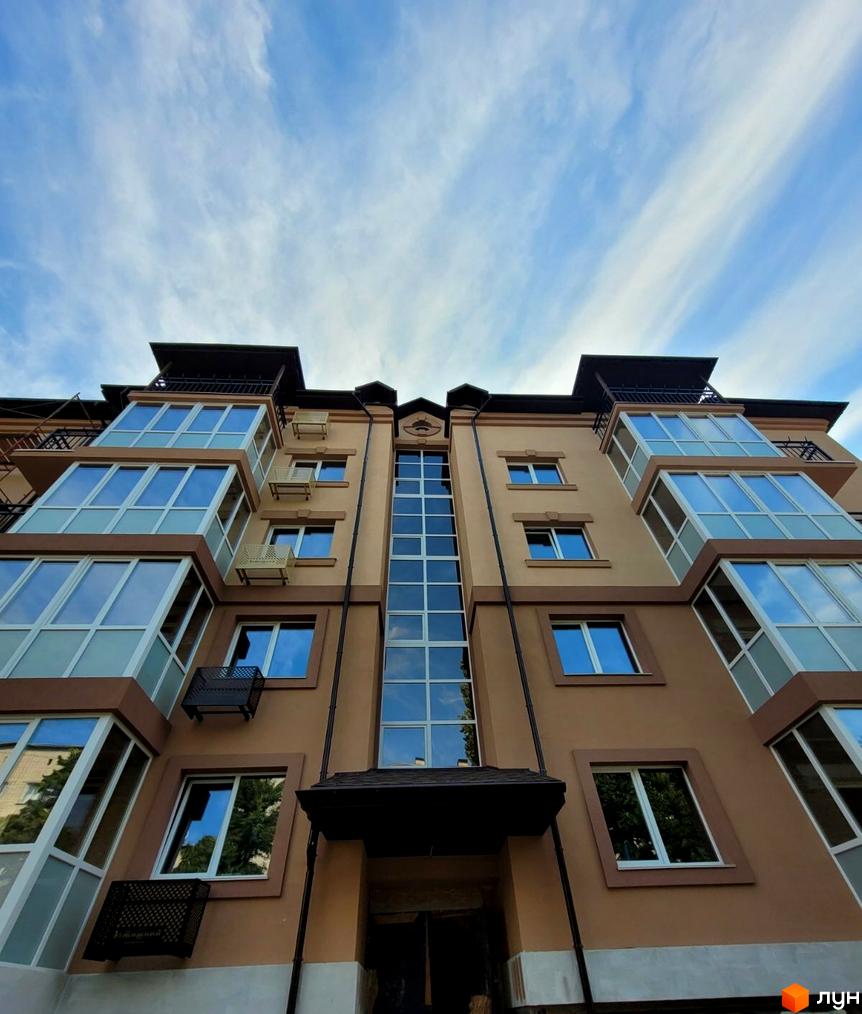 Висока будівля ЖК Затишний з великими вікнами та балконами на фоні блакитного неба з хмарами. Фасад виконано у світлих тонах.