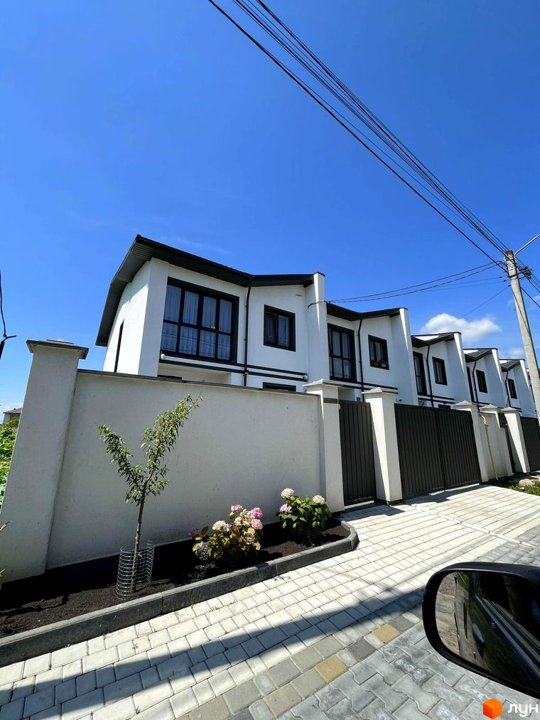 Таунхауси BalHous – це двоповерхові будинки з білими фасадами та темними дахами, розташовані вздовж вимощеної плиткою вулиці з доглянутим ландшафтом.