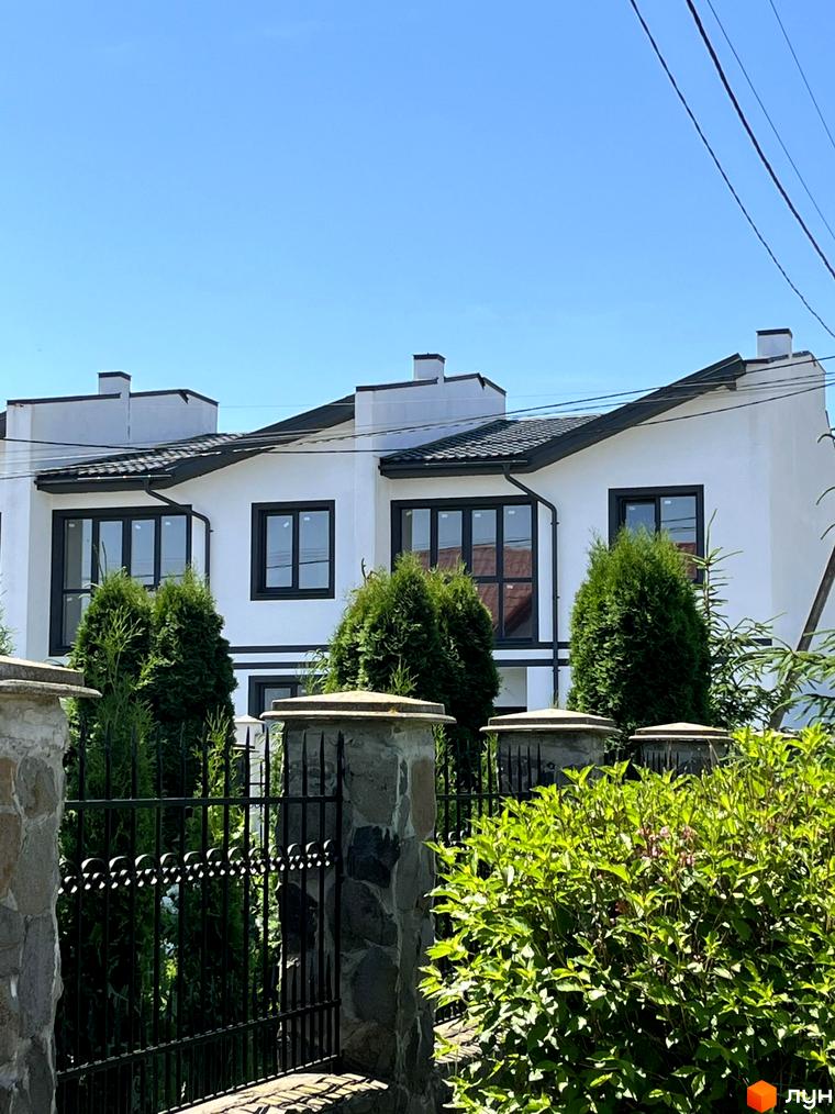 Зовнішній вигляд таунхаусів BalHous з білими стінами та чорними вікнами. На передньому плані огорожа та зелені насадження.