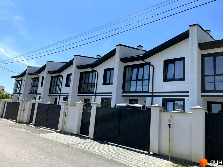 Зображення таунхаусів BalHous з білими стінами та темними вікнами. Перед будинками чорна огорожа та тротуарна доріжка.