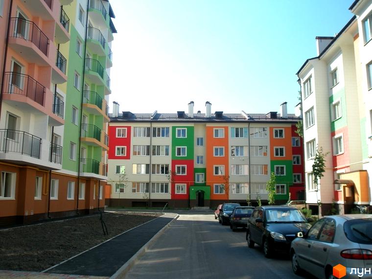 Житловий комплекс Ягода: яскрава фасадна архітектура з балконами та вікнами. Прибудинкова територія з автомобілями та доріжками.