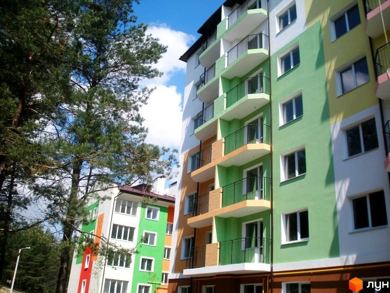 Зовнішній вигляд житлового комплексу ЖК Ягода з яскравими фасадами та балконами. Навколо будівлі розташовані дерева та синє небо з хмарами.