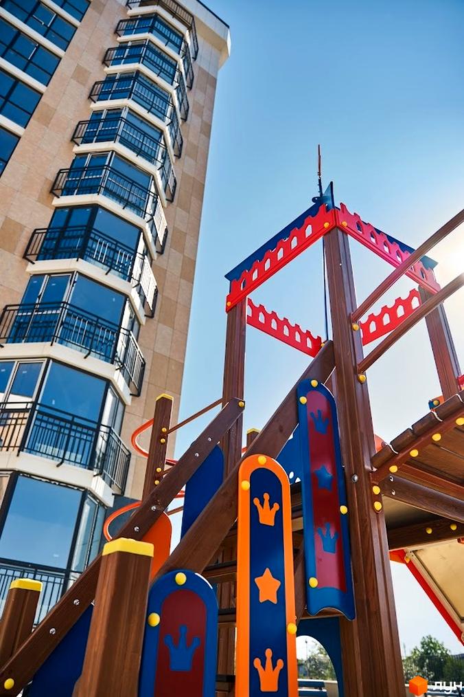 Зображення житлового комплексу Оселя Парк з дитячим майданчиком на прибудинковій території. Вигляд багатоповерхового будинку з балконами.