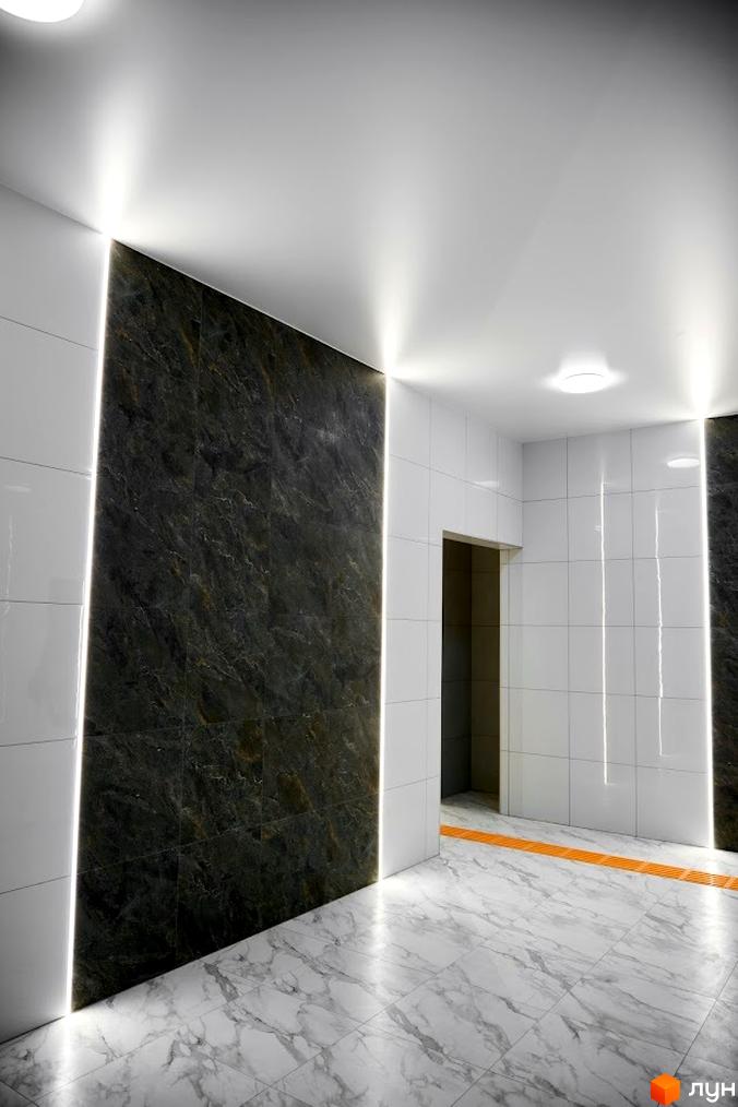 Інтер'єр ЖК Оселя Парк: коридор з мармуровою підлогою та освітленням. Стіни оздоблені плиткою, видно дверний отвір.