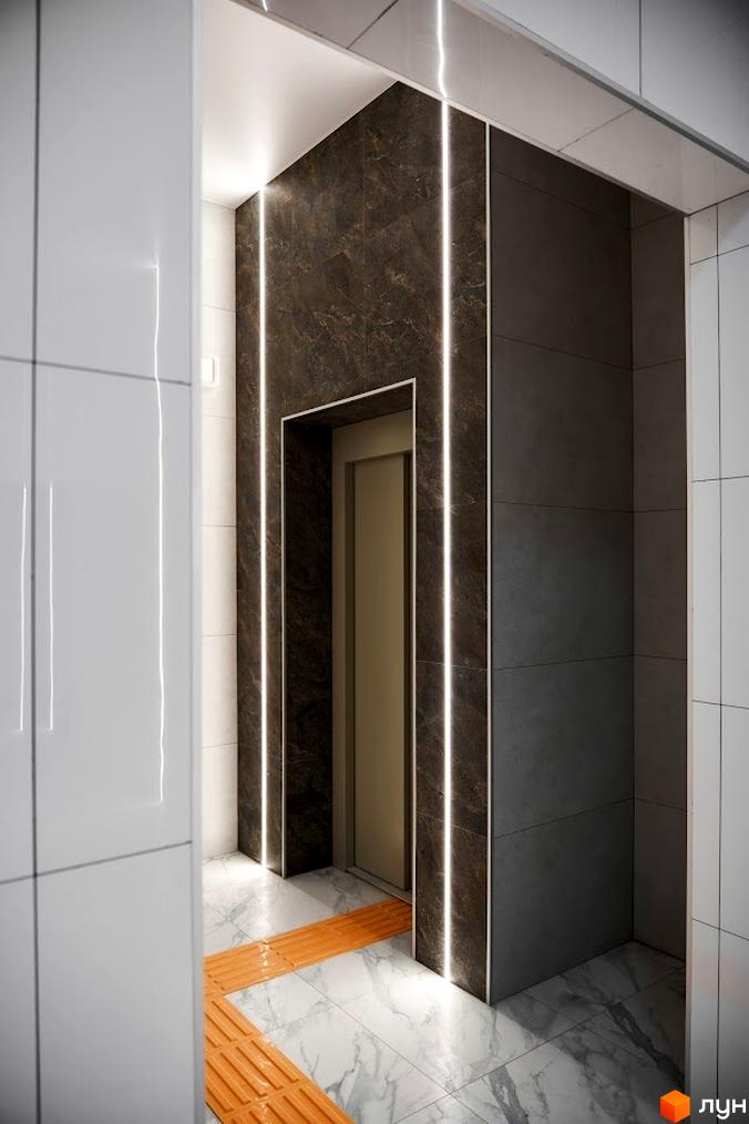 Фото ліфтового холу в Житловому комплексі Оселя Парк. Інтер'єр з використанням плитки та підсвічування, помаранчеві тактильні смуги на підлозі.