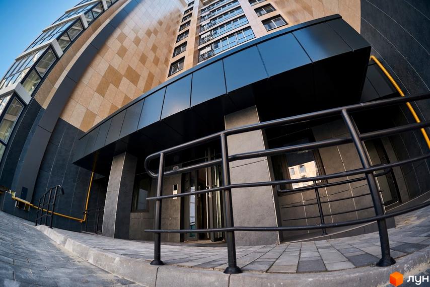 Зображення фасаду та входу в Житловий комплекс Оселя Парк. Вигляд на багатоповерховий будинок з оздобленням та прибудинкову територію.