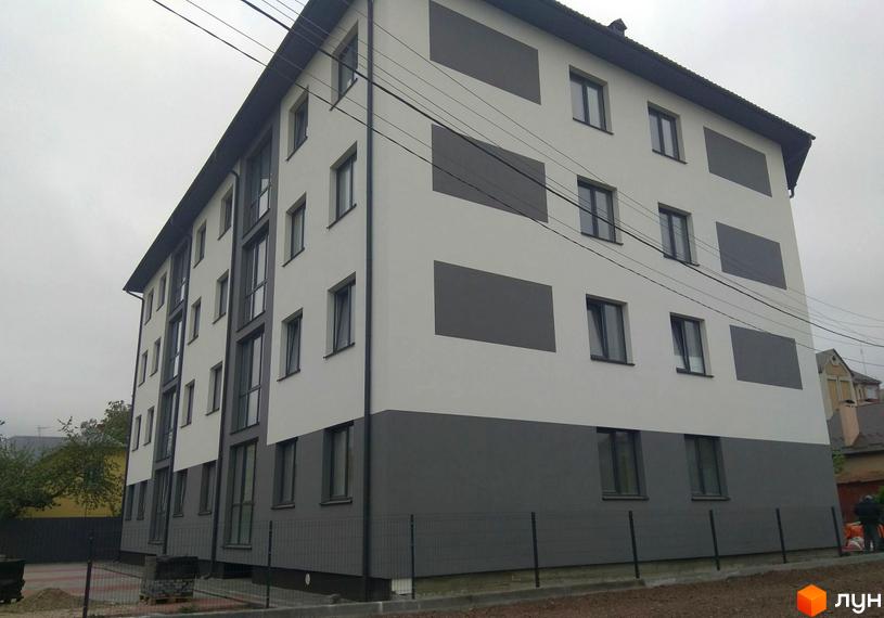 Багатоповерховий будинок з білими та сірими стінами. Поруч розташована огорожа та прибудинкова територія.