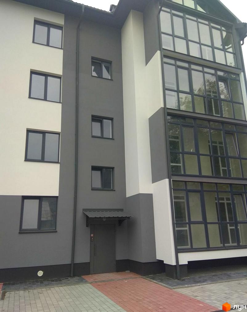 Фасад багатоповерхового будинку з великими вікнами та вхідною групою. Біля будинку викладена бруківка.