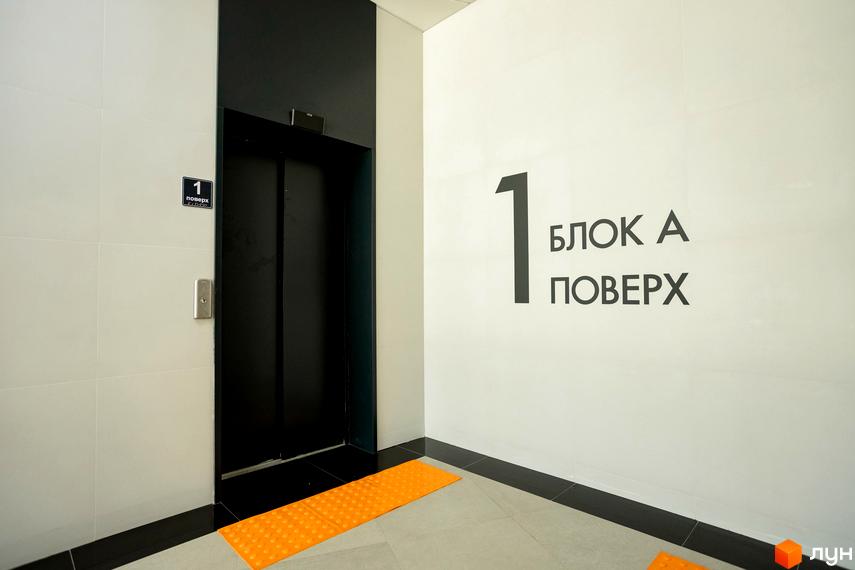 Інтер'єр першого поверху Житлового комплексу Dibrova Park: ліфтовий хол з чорним ліфтом, кнопкою виклику та навігаційними табличками.