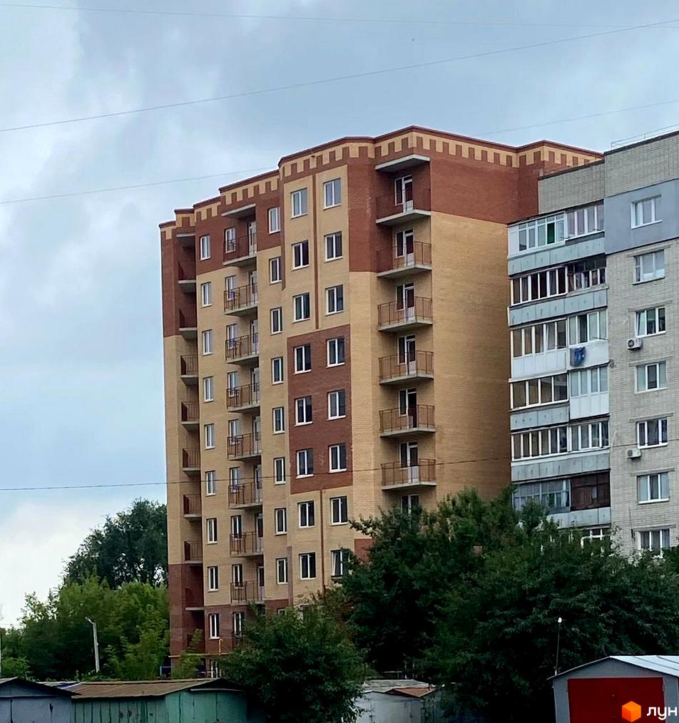 Житловий комплекс Комфорт: багатоповерховий будинок з цегляним фасадом та балконами на тлі дерев.