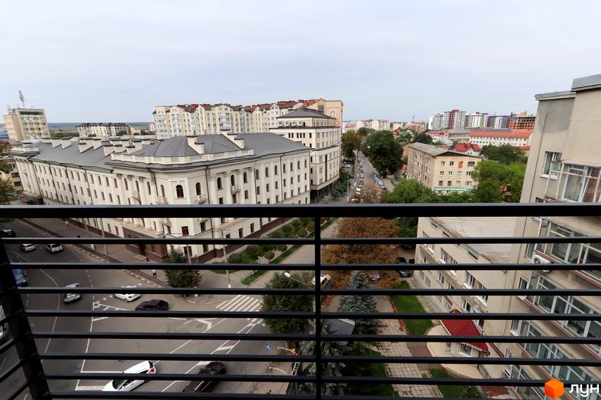 Вид на житловий комплекс Central House з балкона. Будівля має класичну архітектуру з колонами та симетричним фасадом, оточена міським пейзажем з вулицями та іншими будинками.