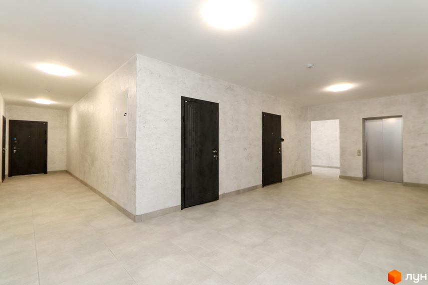 Коридор житлового комплексу Central House з темними дверима та ліфтом. Оздоблення стін та підлоги виконано в світлих тонах.