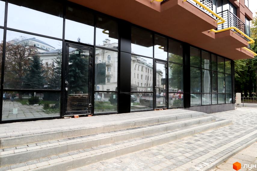 Зовнішній вигляд новобудови ЖК Central House з великими вікнами та дверима, що виходять на вимощену бруківкою територію зі сходами.
