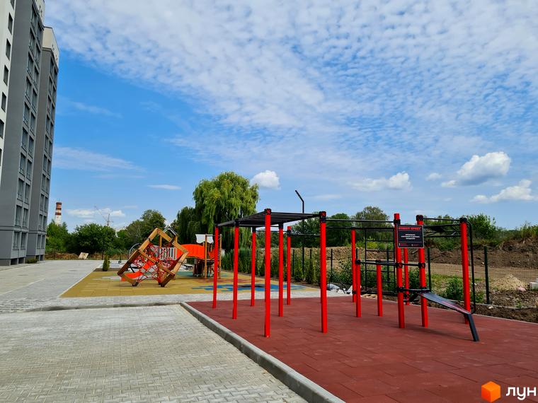 Багатоповерховий будинок Житлового комплексу Дім сірого кольору. Прибудинкова територія облаштована дитячим та спортивним майданчиками.