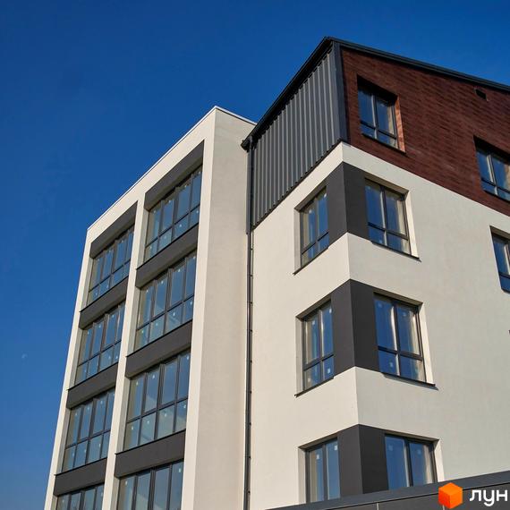 Зовнішній вигляд новобудови ЖК Традиція з великими вікнами та біло-сірим фасадом на фоні блакитного неба. Будівельний проєкт з сучасною архітектурою.