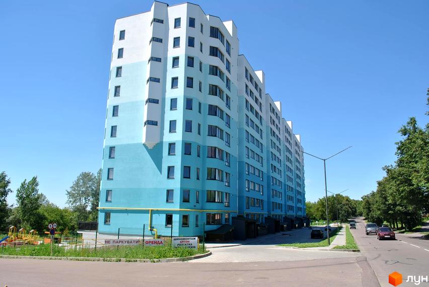 Зображення багатоповерхового будинку у Житловому комплексі Над рікою. На фото фасад будівлі з вікнами та прибудинкова територія з дорогою.