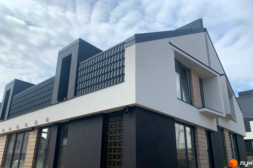 Фасад будинку дуплексів Atlant House з сірим дахом та білими стінами, вікнами та елементами декору. Навколо будинку видно елементи прибудинкової території.