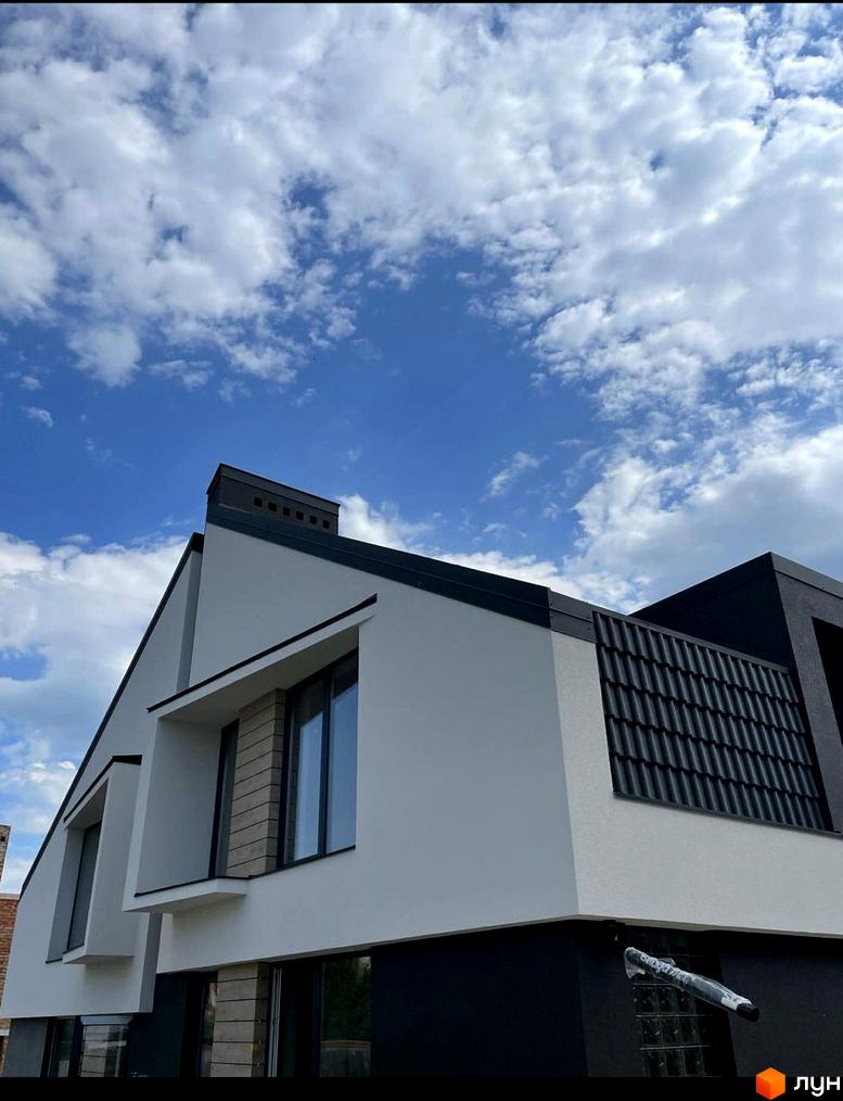 Дуплекси Atlant House - новобудова з білими та темними фасадами, великими вікнами та черепичним дахом під блакитним небом.