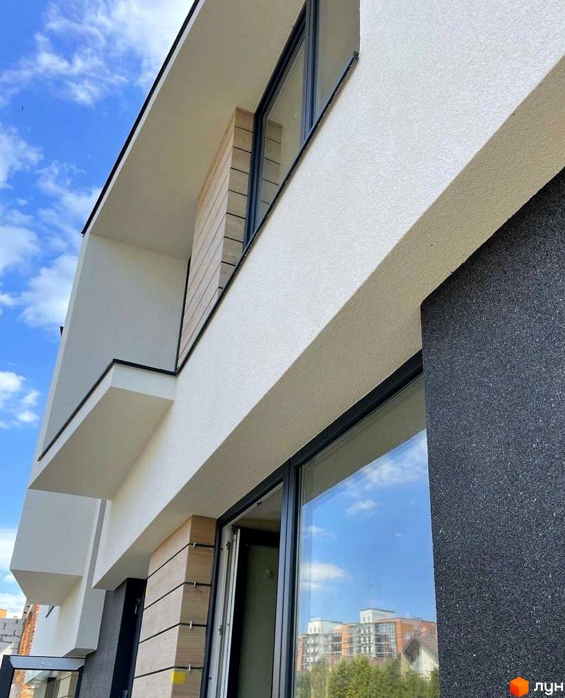 Atlant House - новобудова з білою штукатуркою, дерев'яними елементами та темним фасадом. На вікнах відбивається блакитне небо з хмарами та сусідні будинки.