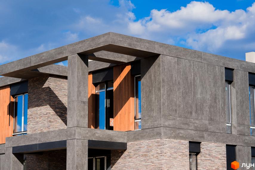 КМ 9 ЕЛЕМЕНТІВ: фасади будинку з сірого каменю та дерева, великі вікна з синіми відблисками неба. Зовнішній вигляд новобудови.