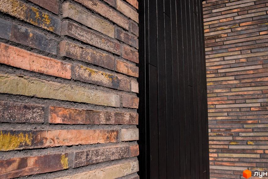 Фасад житлового комплексу КМ 9 ЕЛЕМЕНТІВ оздоблений різнокольоровою цеглою та темними вертикальними панелями. Зовнішній вигляд новобудови з цегляним оздобленням.