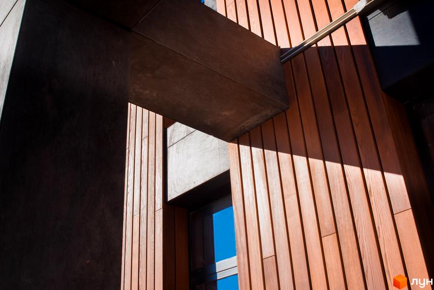 Котеджне містечко КМ 9 ЕЛЕМЕНТІВ. Зовнішній вигляд новобудови з дерев'яним фасадом та бетонними елементами під сонячним світлом.