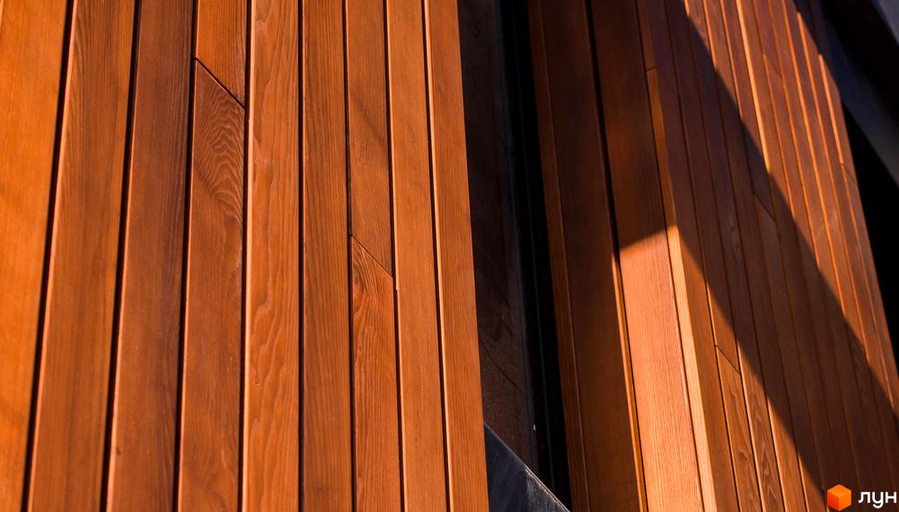 Фасад будинку з дерев'яних панелей у житловому комплексі КМ 9 ЕЛЕМЕНТІВ. Зовнішнє оздоблення новобудови виконане з натуральних матеріалів, що створює затишну атмосферу.