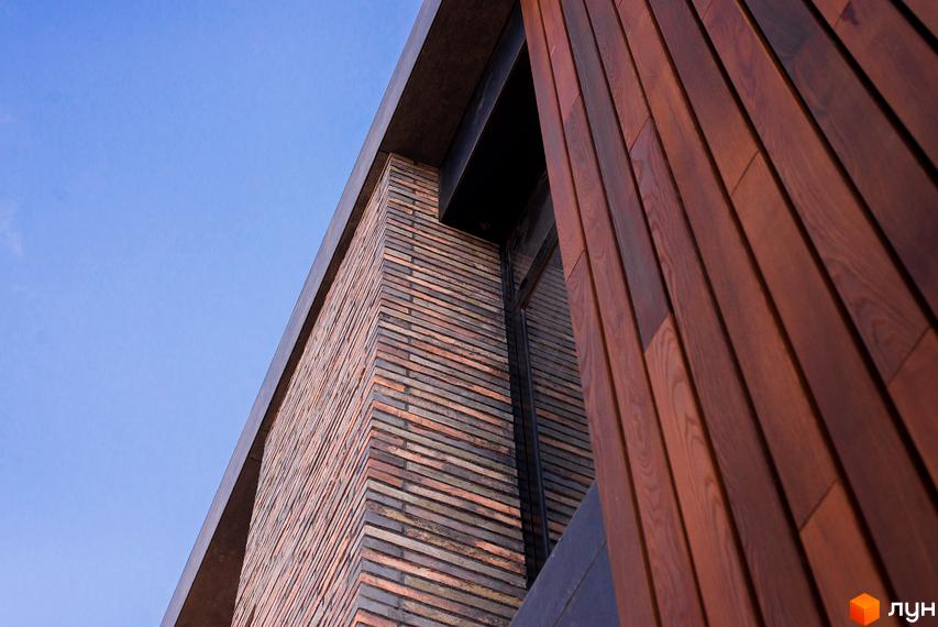 Зовнішній вигляд новобудови КМ 9 ЕЛЕМЕНТІВ з цегляним фасадом та дерев'яними елементами під блакитним небом.