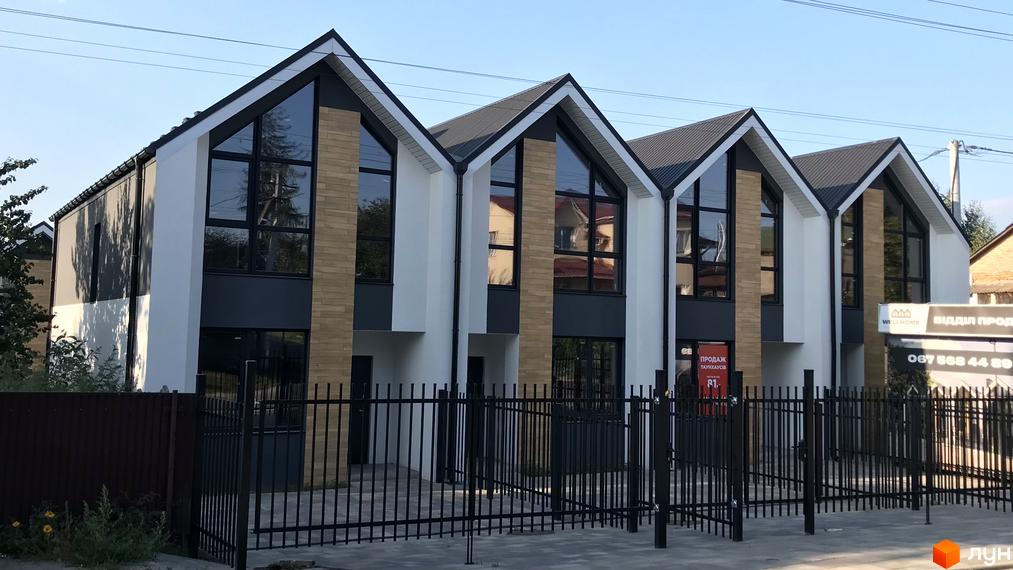 Зовнішній вигляд таунхаусів Well Home з великими вікнами та чорною огорожею. Фасад будинку оздоблений білою штукатуркою та цеглою.