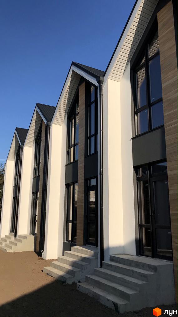 Зовнішній вигляд таунхаусів Well Home з великими вікнами та сходами до входу. Прибудинкова територія з піщаним ґрунтом.