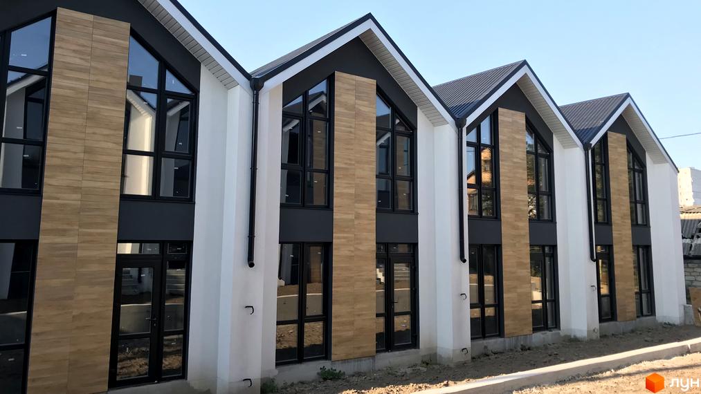 Зовнішній вигляд таунхаусів Well Home з великими вікнами та оздобленням під дерево. Навколо будівельного проєкту облаштована територія.