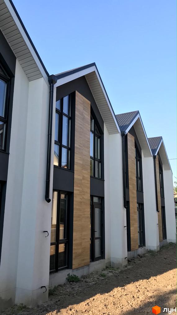 Зображення таунхаусів Well Home з великими вікнами та оздобленням під дерево. Вигляд ззовні на прибудинкову територію.