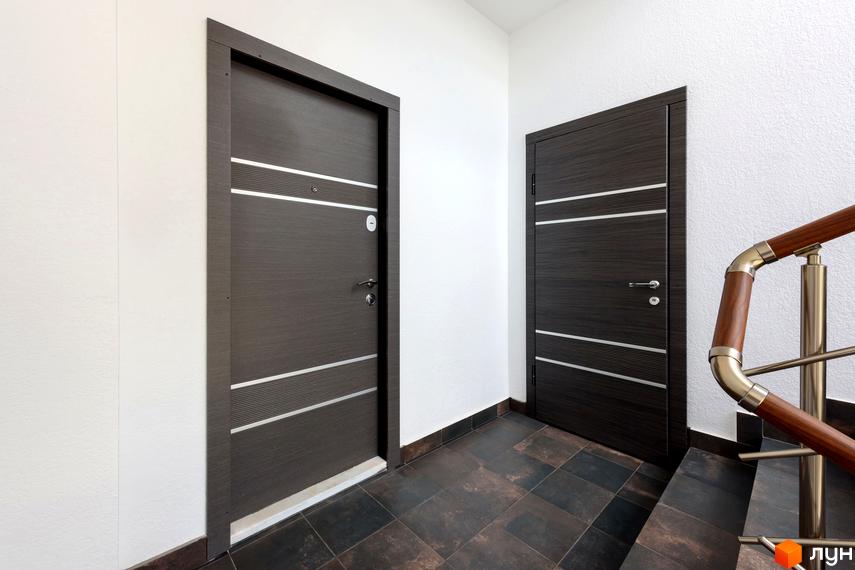 Два темні двері з горизонтальними сріблястими вставками у світлому коридорі з плиткою на підлозі. Вигляд сходової клітки з дерев'яними поручнями.
