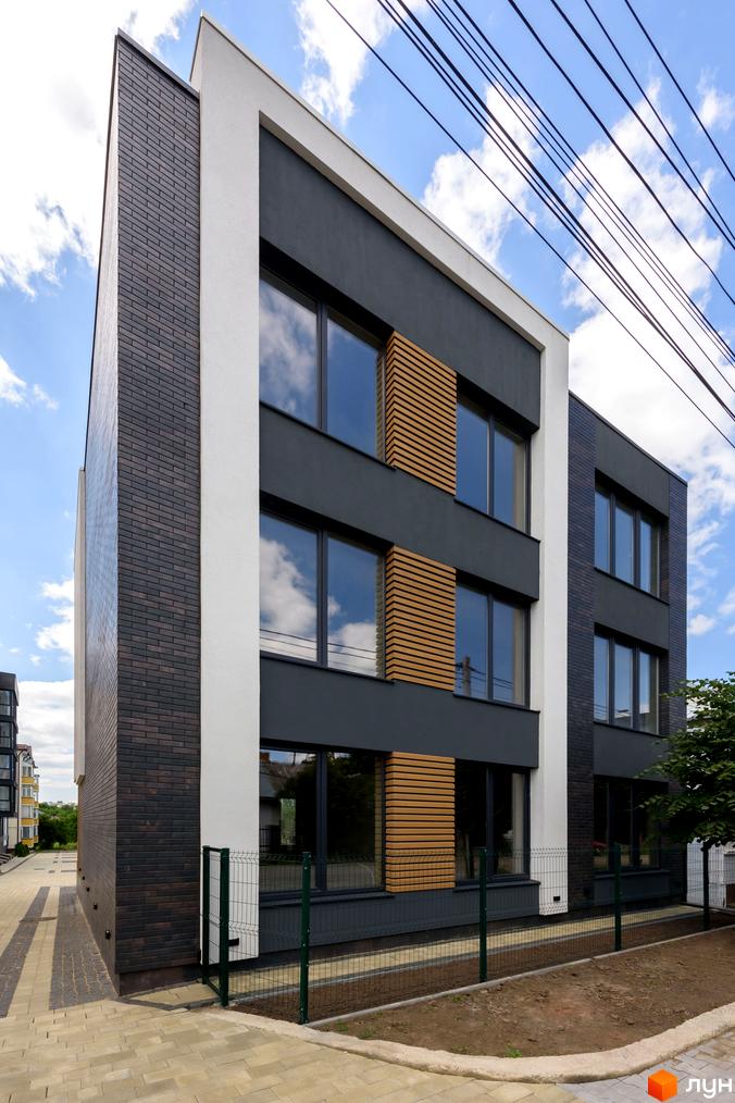 Зовнішній вигляд будинку в Житловому комплексі Elite House з фасадом з цегли та великими вікнами. Навколо будинку зелена територія.