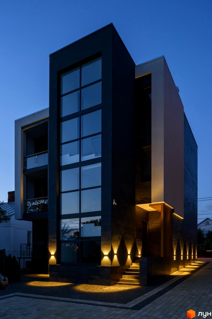 Зовнішній вигляд будинку в Житловому комплексі Elite House з великими вікнами та освітленням. Прибудинкова територія з тротуарною плиткою.