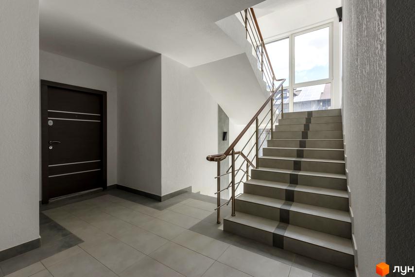 Сучасний під'їзд житлового комплексу Center з темними дверима та сходами з металевим поручнем. Велике вікно відкриває вид на місто.