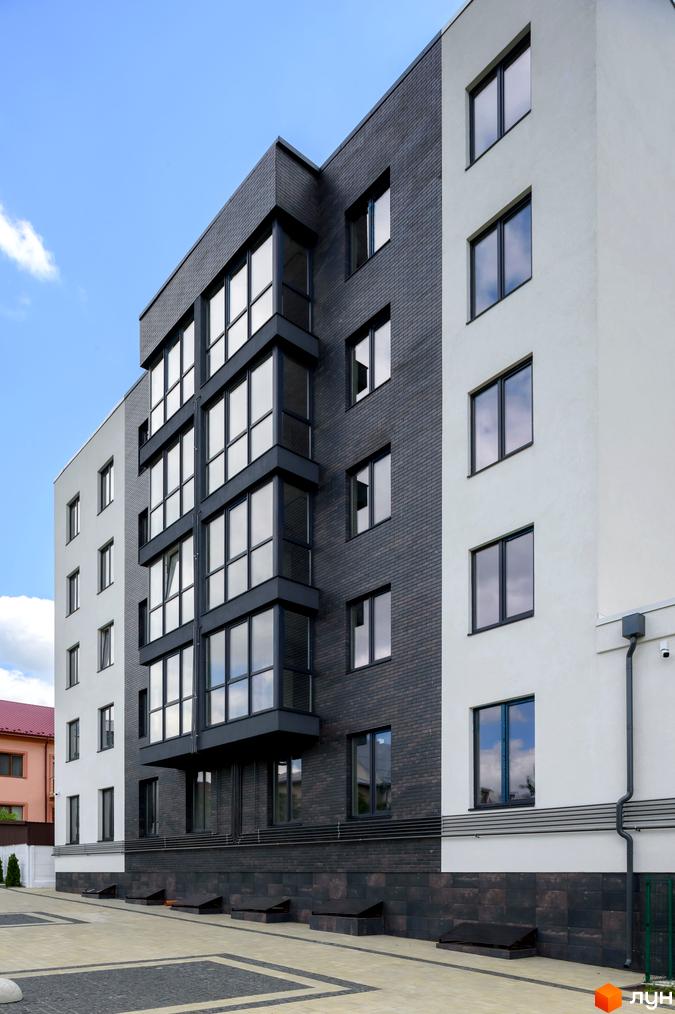 Фасад житлового комплексу Center поєднує білу штукатурку та темну цеглу. Навколо будинку облаштована прибудинкова територія з бруківкою.